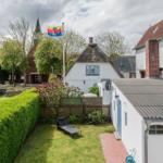 Hinterhof mit Garten, Liegestuhl und Flagge vor einem weißen Haus mit Strohdach.