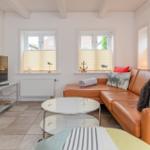 Wohnzimmer mit braunem Sofa, runden Tisch und TV. Zwei Fenster mit Jalousien.