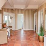 Hausflur mit Streifenwand, Terrakottboden und Sitzgelegenheit unter einer Treppe.