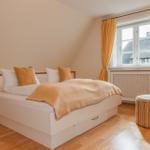 Schlafzimmer mit Doppelbett, gelben Vorhängen und Holzboden. Fenster zeigt Dachhäuser.