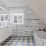 Badezimmer mit Dusche, Badewanne und Fenster. Fliesenboden und weiße Einrichtung.