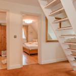 Treppenhaus mit Blick auf Schlafzimmer und Wohnzimmer mit Holzmöbeln und Fenstern.