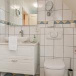 Badezimmer mit Waschbecken, Spiegel und Toilette. Wandfliesen mit dekorativer Bordüre.