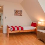 Ein Schlafzimmer mit Holzbett, Sessel und Wandbild. Holzfußboden und Dachschräge.