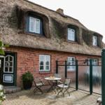Haus mit Strohdach, Terrasse mit Tisch und Stühlen, Eingangstür und Fenster