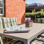 Terrasse mit Tisch, Stühlen und Kaffeetasse. Hintergrund: rote Ziegelwand und Garten.
