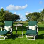 Zwei grüne Liegestühle mit Streifenkissen und Tisch im Gras vor Bäumen.