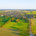 Grünes Feld mit roter Linie, Dorf im Hintergrund, Straße und Bäume