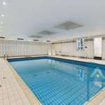 Indoor pool with white benches and blue tiles. Ceiling with lights and window.