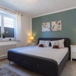 Schlafzimmer mit Bett, zwei Nachttischen und Fenster. Wand in Grün mit Bildern.