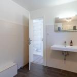 Badezimmer mit Waschbecken, Spiegel und Tür zum Duschbereich.