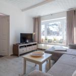 Wohnzimmer mit Sofa, Fernseher und Fenster. Tür führt in den Flur.