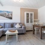 Wohn- und Essbereich mit Sofa, Tisch und Schrank. Wandbilder zeigen Leuchtturm und Strand.