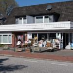 Ein Haus mit Laden im Erdgeschoss und Balkon im Obergeschoss. Vor dem Laden sind verschiedene Artikel ausgelegt.