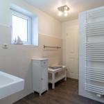 Badezimmer mit Badewanne, Heizkörper und Fenster mit Segelbootmodell.