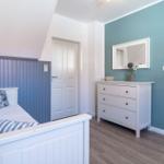 Schlafzimmer mit Bett, Schrank und Spiegel an türkisfarbener Wand.