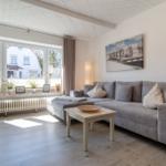 Wohnzimmer mit Sofa, Couchtisch und Fernseher. Fenster mit Blick auf Straße.
