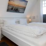 Schlafzimmer mit weißem Bett, Nachttisch und Wandbild. Fenster mit Jalousie.