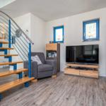 Wohnzimmer mit Fernseher, Sessel und Treppe mit blauen Metallgeländern.