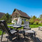 Terrasse mit Tisch, Stühlen und Liegestuhl. Hintergrund: Haus und Grünflächen.