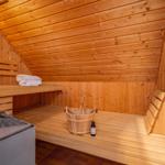 Sauna mit Holzbänken, Eimer und Handtuch. Heizung und Fliesenboden sichtbar.