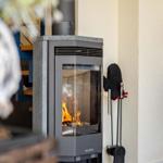 Holzofen mit brennendem Feuer, daneben stehen Ofenhandschuhe und -utensilien.