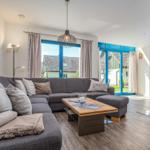 Ein Wohnzimmer mit grauem Sofa, Holztisch und blauen Fenstern.