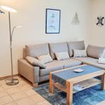 Ein Wohnzimmer mit grauem Sofa, Holz-Tisch und blauem Teppich. Wanddekoration und Vorhänge im Seemannsstil.