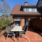Haus mit Terrasse, Tisch, Stühlen und Liegestuhl. Roter Ziegelhof und Dach.