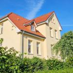 Ein zweistöckiges Haus mit rotem Dach und hellen Wänden, umgeben von Grünflächen.