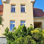 Haus mit gelbem Putz, rotem Dach und grüner Vegetation. Auf der Fassade steht NORDLICHT.