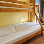 Ein Doppelstockbett mit Holzgestell und weißer Bettwäsche in einem Raum mit Fenster und Heizkörper.