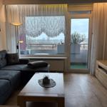 Wohnzimmer mit Sofa, Couchtisch und Balkon. Fenster mit Vorhängen. Fernseher auf Holzschrank.