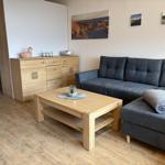 Ein Wohnzimmer mit grauem Sofa, Holztisch und Schrank. Wandbilder zeigen Strand.