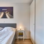 Schlafzimmer mit Bett, Nachttisch und Wandbild. Kleiner Schrank an der Wand.