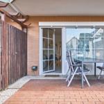 Terrasse mit Tisch und Stühlen, Glasfront zur Wohnung, Holzgeländer und Ziegelsteinmauer.
