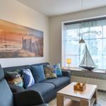 Wohnzimmer mit Sofa, Couchtisch und Fenster mit Blick. Wandbild zeigt Strand.