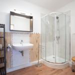 Badezimmer mit Dusche, Waschbecken und Toilette. Holzoptik an Wänden und Boden.