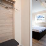 Schlafzimmer mit Bett und Fenster. Ankleidebereich mit Kleiderständer und Sitzbank.