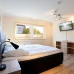 Schlafzimmer mit Doppelbett, Fenster, Fernseher und Nachttisch.