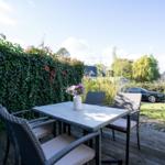 Terrasse mit Tisch und Stühlen, umgeben von grüner Hecke und Garten.