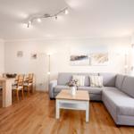 Wohn- und Essbereich mit grauem Sofa, Holztisch und Fensterblick.