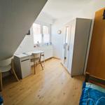 Schlafzimmer mit Schreibtisch, Kleiderschrank und Fenster. Holzboden und Tür mit Aufkleber.