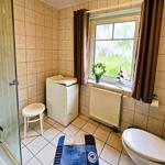 Bathroom with shower, washing machine, toilet, and window with curtains.