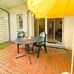 Terrace with table, two chairs, and yellow umbrella. Through glass doors, the apartment is visible.