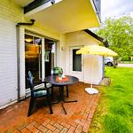 Terrace with table, two chairs, and yellow umbrella. Background: green lawn and tree.