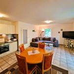 Living and dining area with kitchenette, sofa, and TV. Wooden table with four chairs.