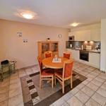 Dining room with round table, four chairs, and kitchen area with white cabinets.