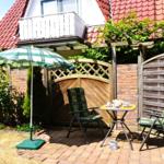 Terrace with table, two chairs, and umbrella. Background: wooden gate, fence, and house with red roof.