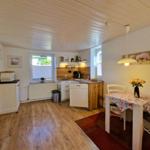 Kitchen with dining area, wooden floor, and windows. Table with tablecloth and flowers.